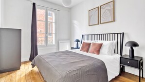 A modern bedroom with a large bed, a nightstand, a lamp, and two wall art pieces. - Blueground | Bastille, elevator, nr Charonne (Paris)