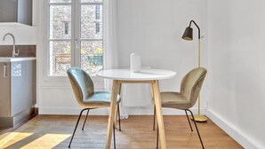 A modern kitchen with a round dining table, two chairs, a floor lamp, and a view of a stone building through a window. - Blueground | Bastille, elevator, nr Charonne (Paris)