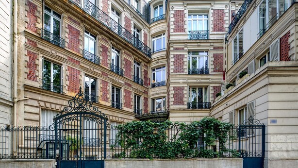 A multi-story building with a central courtyard, featuring a wrought iron gate and a concrete wall with a metal fence. - Blueground | Porte de Champerret, furnished (Paris)