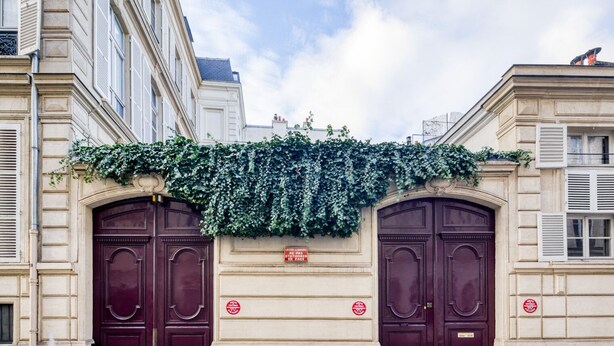 A building facade with two symmetrical dark red doors, a sign indicating a garage entrance, and a vine-covered wall. - Blueground | Invalides, concierge, a/c, nr museums (Paris)