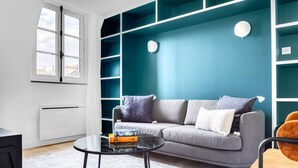 A modern living room with a grey sofa, a glass coffee table, and a teal accent wall. - Blueground | Invalides, concierge, a/c, nr museums (Paris)