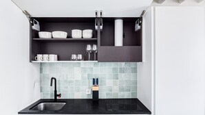 A modern kitchen with a black countertop, stainless steel sink, and a backsplash with light blue tiles. - Blueground | Invalides, concierge, a/c, nr museums (Paris)