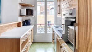A modern kitchen with wooden cabinets, a white countertop, and a view of the outside balcony. - Blueground | Montparnasse, concierge, nr train (Paris)