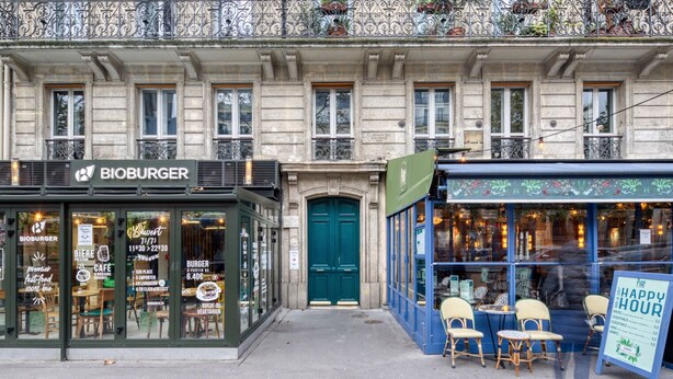 A building with a restaurant named 'BIOBURGER' on the ground floor, featuring a green door and outdoor seating. - Blueground | Montparnasse, concierge, nr train (Paris)