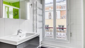 A modern bathroom with a white sink, a mirror, and a view of a balcony with a railing. - Blueground | Montparnasse, concierge, nr train (Paris)
