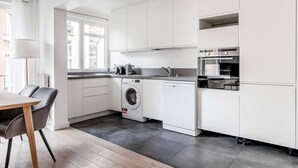 A compact kitchen with white cabinetry, a washing machine, a dishwasher, and a built-in oven. - Blueground | Villiers/Batignolles, nr shops (Paris)