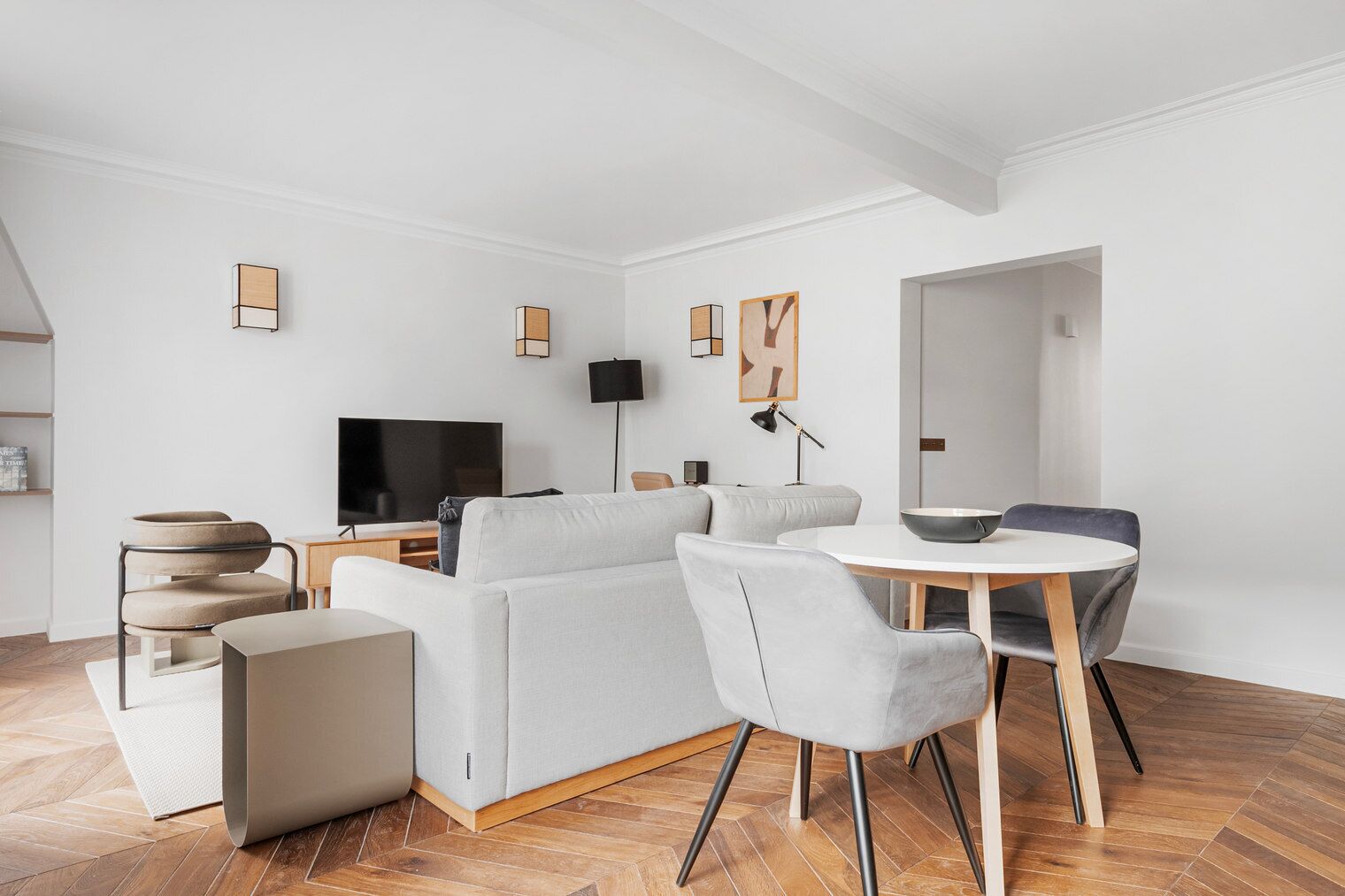A modern living room with a sofa, a TV, a dining table with chairs, and a lamp.