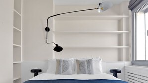 A bedroom with a bed, two bedside tables, a wall-mounted reading lamp, and built-in shelving. - Blueground | Chardon Lagache, balcony & concierge (Paris)