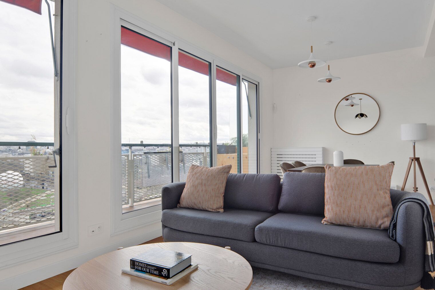 A modern living room with a grey sofa, a round coffee table, and a book titled 'Homes for Our Time'.