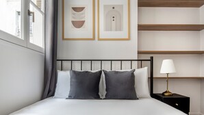 A modern bedroom with a bed, bedside tables, and framed artwork on the wall.