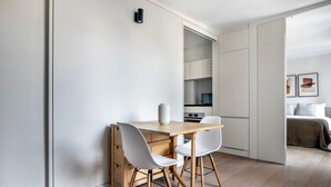 Una cocina compacta y moderna con una mesa de madera y sillas blancas, horno empotrado y microondas.