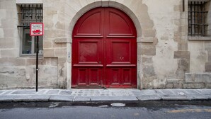 Una puerta roja con un arco de entrada, fachada de un edificio de piedra y un cartel que indica zona de no estacionamiento.