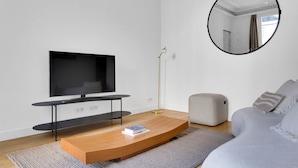 A modern living room with a flat-screen TV, a round mirror, a grey sofa, and a wooden coffee table.