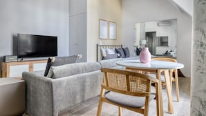 A modern living room with a grey sofa, a round wooden table, and a television on a cabinet. - Blueground | George V, security, nr Champs Elysées (Paris)