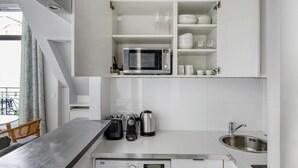 A modern kitchen with white cabinetry, a built-in microwave, a coffee maker, a kettle, and a sink. - Blueground | George V, security, nr Champs Elysées (Paris)