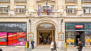 A building with a large arched entrance, banners, and storefronts including a Levi's store. - Blueground | George V, security, nr Champs Elysées (Paris)