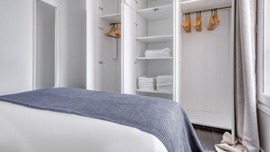 A modern bedroom with a bed, a walk-in closet with shelves and hanging space, and a window with curtains. - Blueground | Champ de Mars, nr Eiffel Tower (Paris)