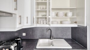 A modern kitchen with a built-in sink, a stove, and open cabinets displaying dishes and glasses. - Blueground | Champ de Mars, nr Eiffel Tower (Paris)
