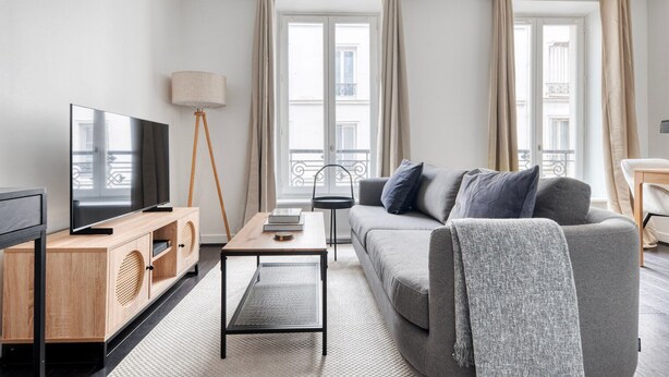A modern living room with a flat-screen TV, wooden entertainment unit, a small table, a sofa with cushions, and a floor lamp. - Blueground | Champ de Mars, nr Eiffel Tower (Paris)