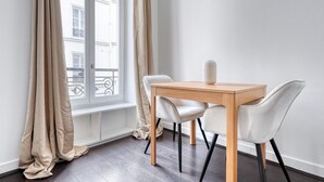 A modern room with a wooden table and two chairs, a window with curtains, and a view of buildings outside. - Blueground | Champ de Mars, nr Eiffel Tower (Paris)