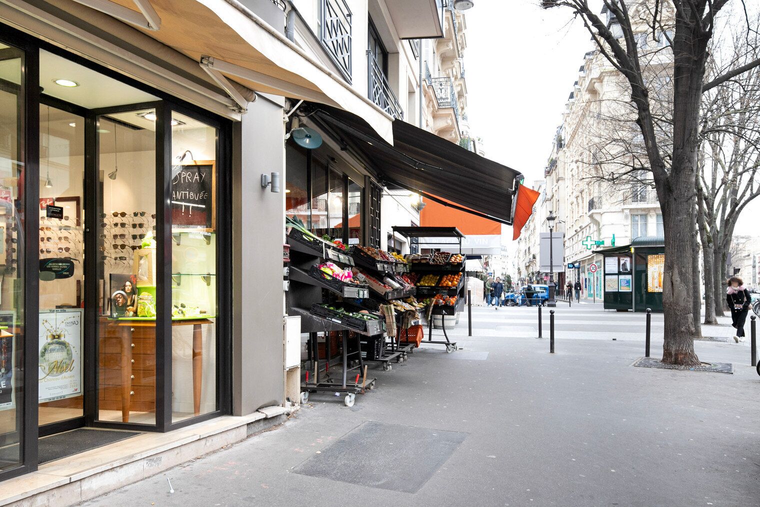 A street view with a storefront displaying various items and a market stall with fresh produce.