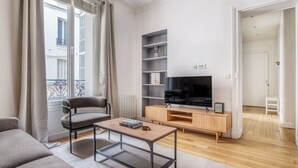 A modern living room with a sofa, coffee table, TV, and built-in shelving. - Blueground | Batignolles, office & intercom (Paris)