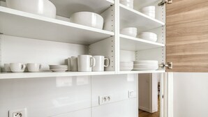 A white kitchen with white cabinets, shelves with dishes and cups, and a wooden door. - Blueground | Batignolles, office & intercom (Paris)