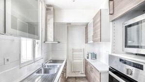 A modern kitchen with stainless steel appliances, a built-in oven, and a microwave. - Blueground | Batignolles, office & intercom (Paris)