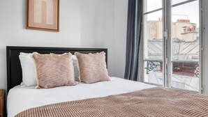 A bedroom with a large bed, two pillows, a framed picture on the wall, and a view of buildings through a window. - Blueground | Notre Dame de Lorette, nr opera (Paris)