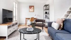 A modern living room with a flat-screen TV, a coffee table, a sofa, a desk with a chair, and a bookshelf. - Blueground | Notre Dame de Lorette, nr opera (Paris)