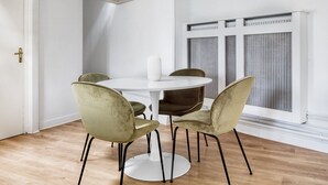 A dining area with a round table and four chairs, a white vase on the table, and a window with blinds. - Blueground | Notre Dame de Lorette, nr opera (Paris)