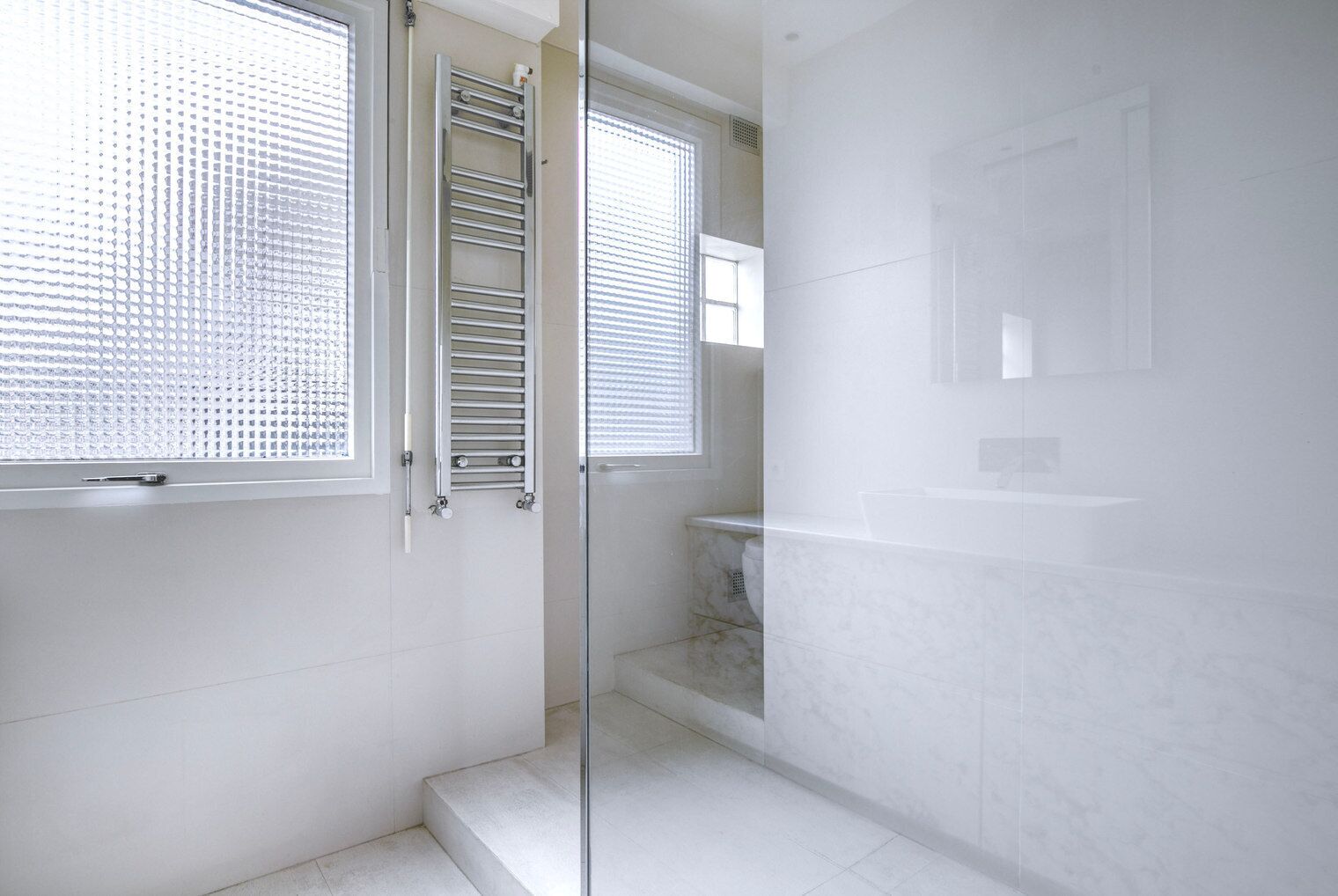A modern bathroom with a glass shower enclosure, white tiles, and a toilet.