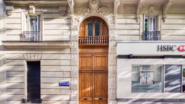 Eine Gebäudefassade mit einer großen Holztür und einem Schild mit der Aufschrift "RUE CAULAINCOURT", sowie einer HSBC Bankfiliale.