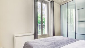 Ein Schlafzimmer mit einem Bett, einem Fenster mit Vorhängen, einem Heizkörper und einem Kleiderschrank.