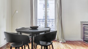 Ein Essbereich mit einem runden Tisch und vier Stühlen, einer Schüssel auf dem Tisch, einer Stehlampe und Blick auf einen Balkon mit Metallgeländern.