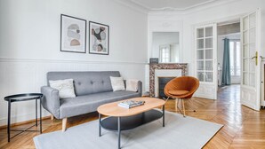 A living room with a grey sofa, a round coffee table, a small side table, and a fireplace. - Blueground | Levallois Perret, nr dining (Paris)