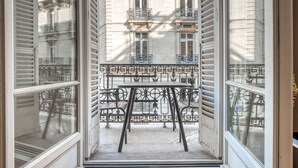A narrow balcony with a table and chairs, overlooking a building with ornate balconies and windows. - Blueground | Champs Elysées, furnished, balcony (Paris)