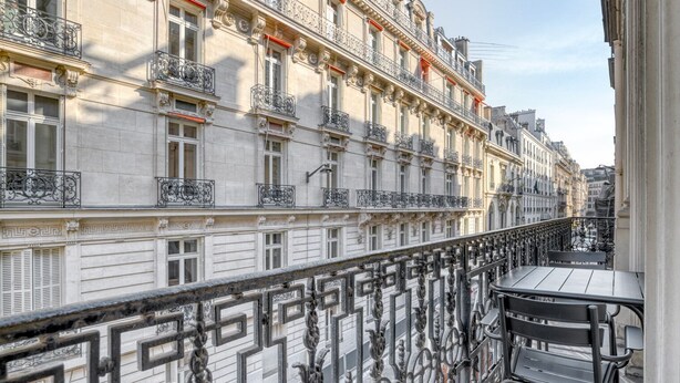 A balcony with ornate wrought iron railings, a table, and a bench. - Blueground | Champs Elysées, furnished, balcony (Paris)