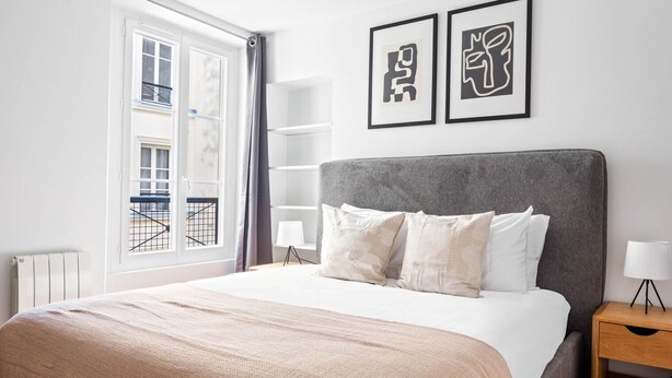 A neatly arranged bedroom with a large bed, a grey headboard, and two framed artworks on the wall. - Blueground | Montorgueil, intercom, nr Les Halles (Paris)
