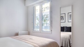 A bedroom with a bed, a window with a view of buildings, and a mirror reflecting the bed and window. - Blueground | Le Marais, concierge & elevator (Paris)