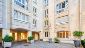 A multi-story building with a courtyard. There are potted plants and a small tree in the courtyard. - Blueground | Le Marais, concierge & elevator (Paris)