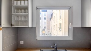 A kitchen with a built-in window, grey tiles, a sink, and shelves with glassware. - Blueground | Le Marais, concierge & elevator (Paris)