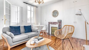 A modern living room with a grey sofa, a wicker chair, a round coffee table, and a fireplace. - Blueground | Le Marais, nr Saint Paul (Paris)