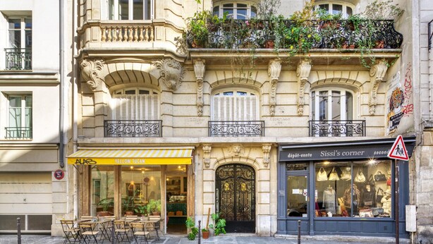 A historic building with ornate balconies, a café named 'Yellow Tucan' on the ground floor, and a store named 'Sissi's corner' on the second floor. - Blueground | Le Marais, nr Saint Paul (Paris)