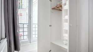 A room with a large window, a wardrobe with hanging space, and a shelf with folded towels. - Blueground | Invalides, elev, nr historic museums (Paris)