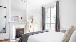 A bedroom with a large bed, a fireplace, a mirror, and a view of the outside through a window. - Blueground | Invalides, elev, nr historic museums (Paris)