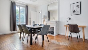A dining area with a wooden herringbone floor, a round table with chairs, a fireplace, and a desk with a chair. - Blueground | Invalides, elev, nr historic museums (Paris)