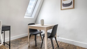 Una habitación pequeña y moderna con techo inclinado, tragaluz, una sencilla mesa de madera con dos sillas y un cuadro minimalista en la pared.