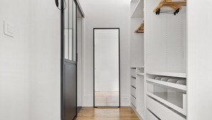 Un couloir étroit avec un plancher en bois, des murs blancs et une porte au fond.