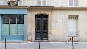 Une façade d’immeuble avec une porte cintrée de couleur sombre, une fenêtre bleue et un petit balcon doté d’une rambarde en métal.